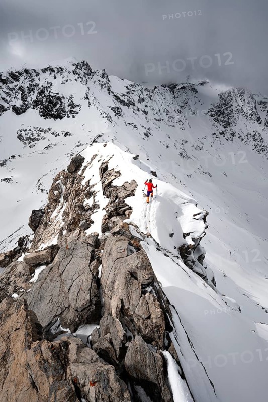 Mountaineer descending the narrow ridge of Piz Laviner, view of mountain panorama in wintry mountain landscape with dramatic clouds, Grisons Haute Route, Albula Alps, Rhaetian Alps, Grisons, Eastern Switzerland, Switzerland