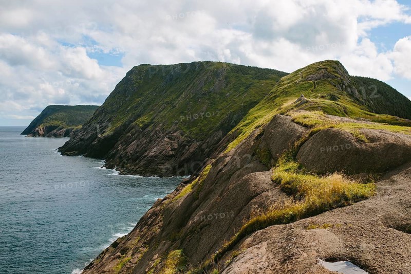 Panoramic view of the rugged cliffs and ocean at Signal Hill, Middle Cove, Newfoundland & Labrador, Canada. The lush greenery and dramatic coastlines under a partly cloudy sky offer a natural escape