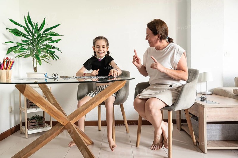 A loving family shares a joyful moment with a mother playing puzzle with disabled girl who has a tracheostomy