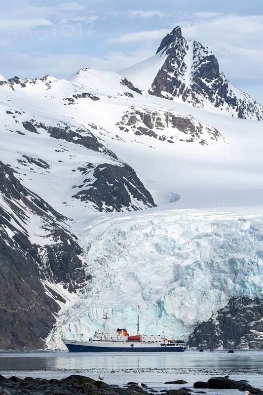 Expedition ship Ushuaia anchors in front of glacier front, snow-capped mountain peaks in the background, Drygalski Fjord, South Georgia