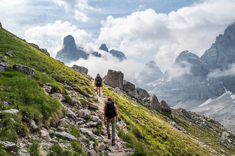 Two mountaineers on a hiking trail in front of a picturesque mountain landscape with rocky peaks, Via Ferrata SOSAT via ferrata, summit of Cima Tosa in the back, Brenta Mountains, Trentino, Italy