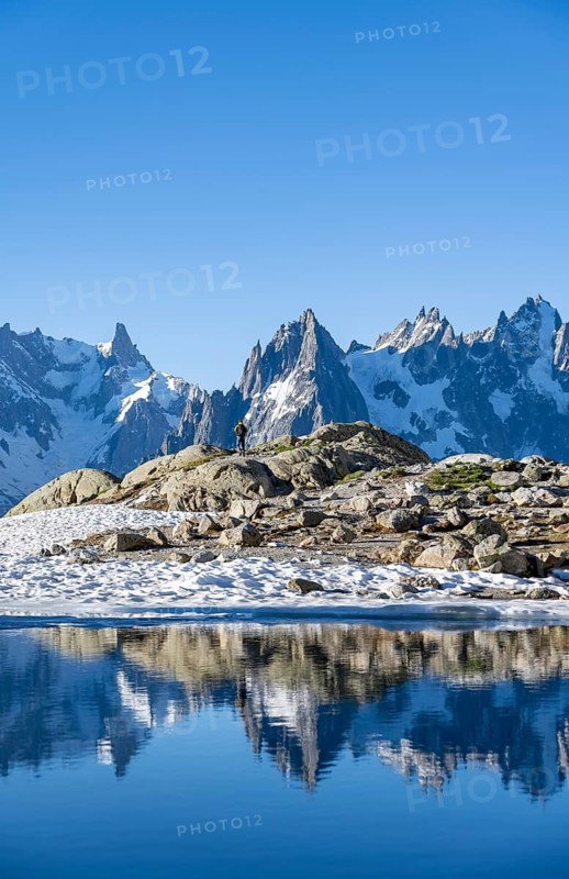 Young man in front of impressive mountain landscape in morning light, reflection in the Lac Blanc mountain lake, mountain summit, Aiguille Verte, Grandes Jorasses, Aiguille du Moine, Mont Blanc, Mont Blanc Massif, Chamonix-Mont-Blanc, Haute-Savoie, France