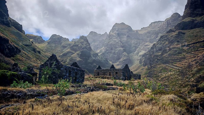 Stone ruins of old houses made of volcanic stone against a spectacular mountain backdrop with thick clouds, hiking, lost place, abandoned village of Formiguinhas, Marinha da Cruzinha Natural Park, Santo Antao, Cabo Verde, Cape Verde, Cape Verde