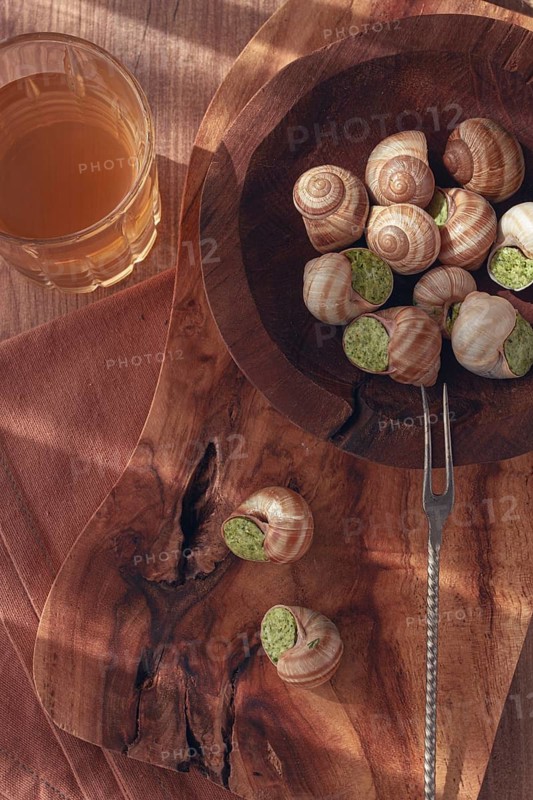 Snails cooked with herb oil on a wooden plate, served with white wine, natural light, no people