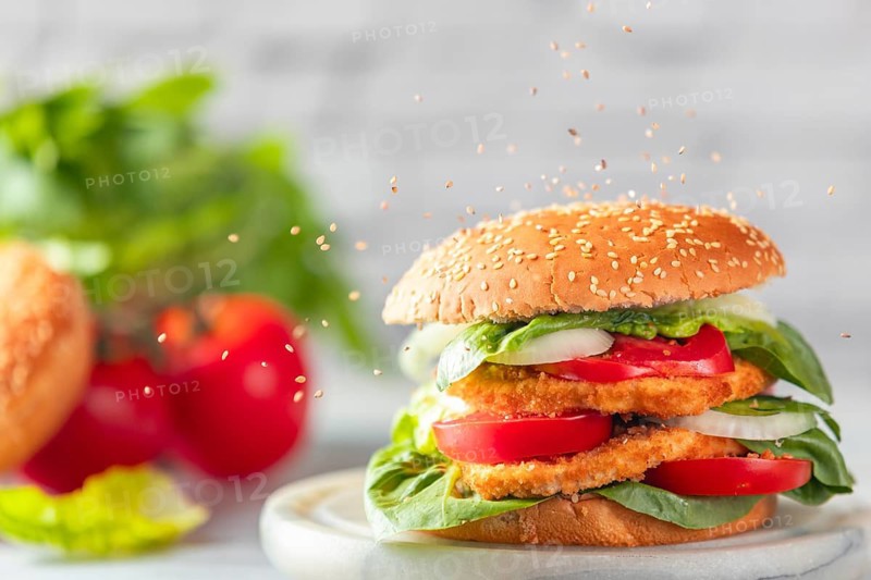 Sesame falls on burgers with vegan schnitzel, tomatoes, onions and salad with ingredients in the background