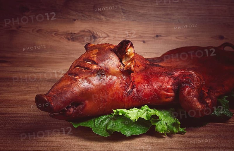 Baked, fried piglet, on a wooden table, no people, The whole piglet is baked and served on the leaves of a fresh green salad, showing off its crispy skin and detailed features