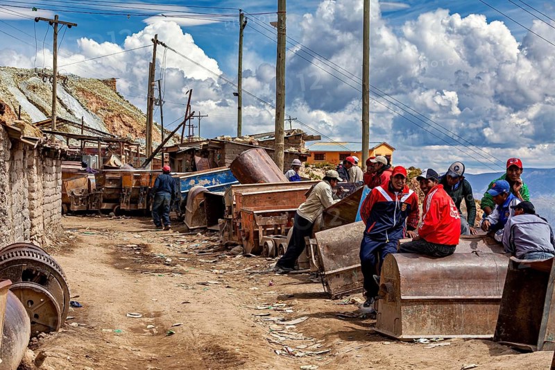 People sit at carts in a dusty street with buildings and telephone lines in the background, The Potosi silver mines on Cerro Rico in Bolivia