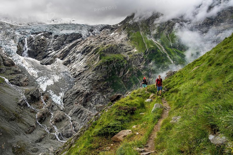 Two mountaineers on a hiking trail, cloudy mountain landscape with Grindelwald-Fiescherfirn glacier, Bernese Alps, Bernese Oberland, Switzerland