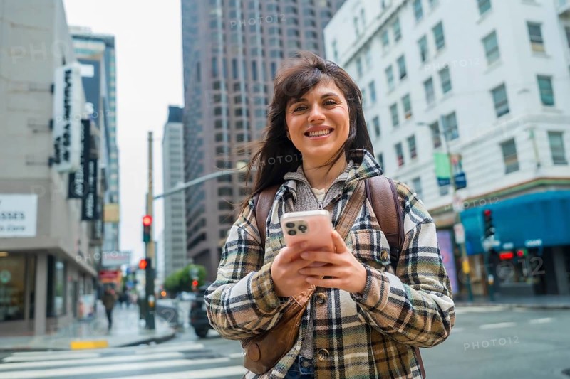 Young woman confidently navigating san francisco's urban environment, smiling while holding a smartphone, representing connection, travel, and modern city life while crossing a street