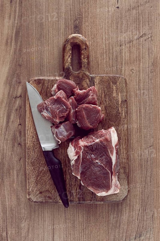 Raw beef meat, sliced on a cutting board, with a knife, no spices, no herbs, top view, wooden table, homemade, no people