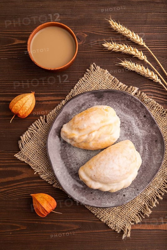 Glazed Pies with Cowberry jam on brown wooden background and linen textile, cup of coffee, top view, flat lay, close up