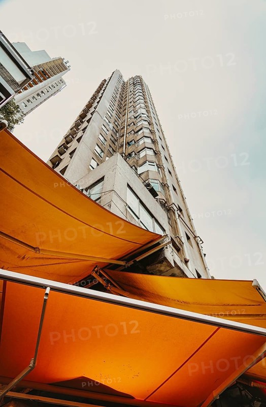 From below high-rise building framed by vibrant yellow awnings on a cloudy day in Hong Kong, showcasing urban architecture and design