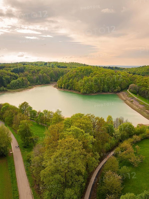 Idyllic lake with surrounding forest and winding paths under a cloudy sky, Glems reservoir, Swabian Alb, Germany