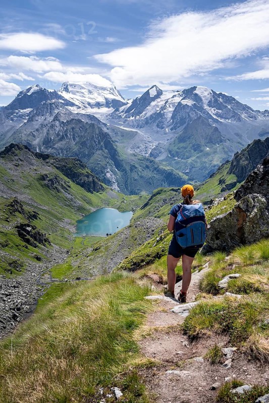 Hiker on hiking trail, mountain lake Lac de Louvie with glaciated summit of the Grand Combin, Val de Bagnes, Valais, Switzerland
