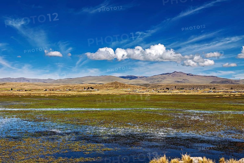 Open landscape with a water area in the foreground, surrounded by hills and a blue sky, The villages and countryside near Puno in Peru