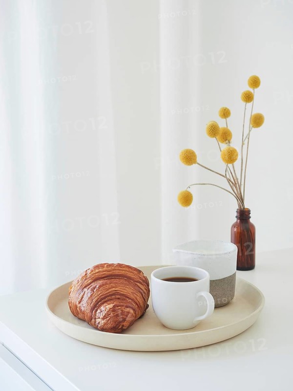 Minimalist lifestyle composition for breakfast. Tray with coffee cup, milk jug, croissant and amber bottle with yellow flowers