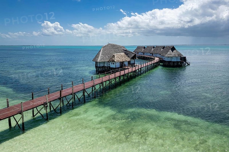 Luxury overwater wooden boardwalk and traditional thatched bungalows spanning across the crystal clear turquoise ocean at a tropical resort in Zanzibar