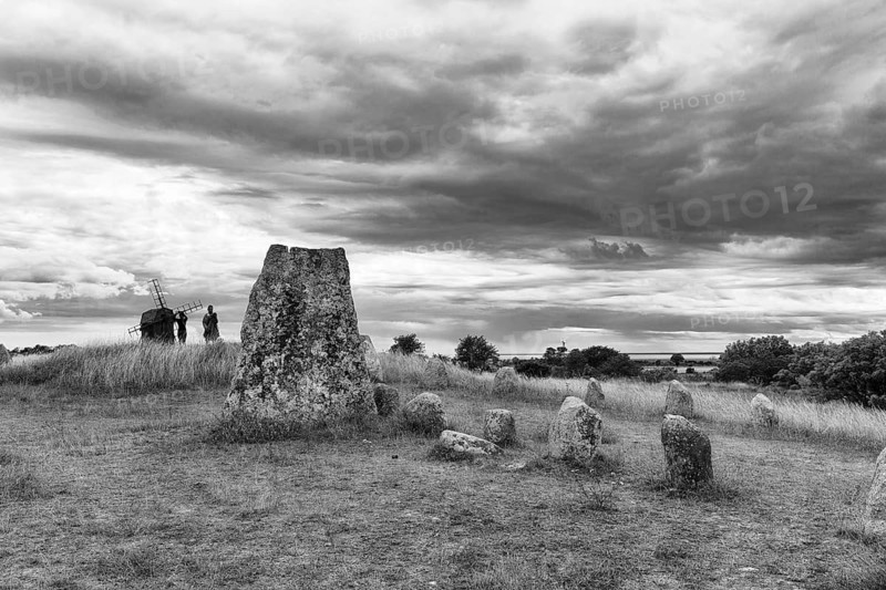 Granite block, burial ground from the Iron Age and Viking Age, stone rows, shipwreck, walkers in barren limestone landscape, Stora Alvaret, UNESCO World Heritage Site, agricultural landscape of South Öland, dramatic cloudy sky, monochrome, Gettlinge, Südoeland, Öland island, Kalmar län, Sweden