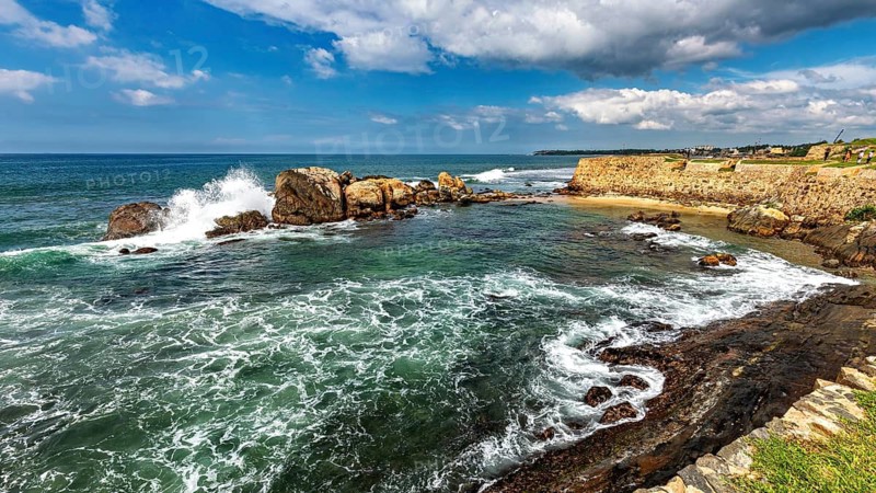 Coastal landscape with waves crashing against rocks under a cloudy blue sky, The rocky coast in the Indian Ocean near Galle in Sri Lanka