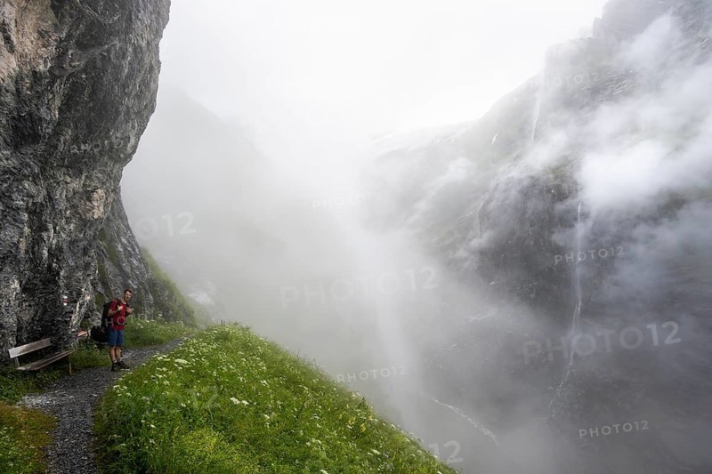 Mountaineer hiking on a hiking trail on a steep rock face, hiking to Berghaus Bäregg, cloud-covered rock gorge with waterfall, Bernese Alps, Bernese Oberland, Switzerland