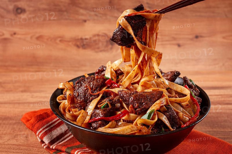 Udon noodles with beef in Mongolian style, with green onions and vegetables, served in a black bowl, on a wooden table, homemade, no people