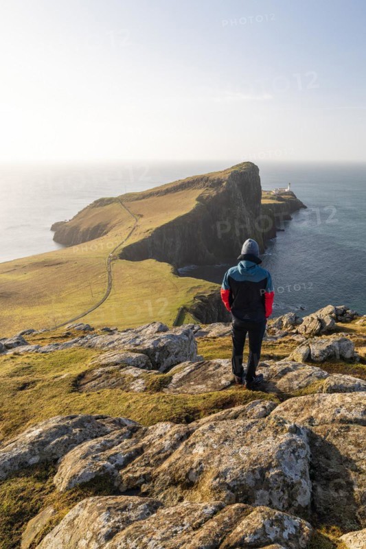 A walker looks up at Neistpoint Lighthouse in the morning light, Isle of skye, Great Britain