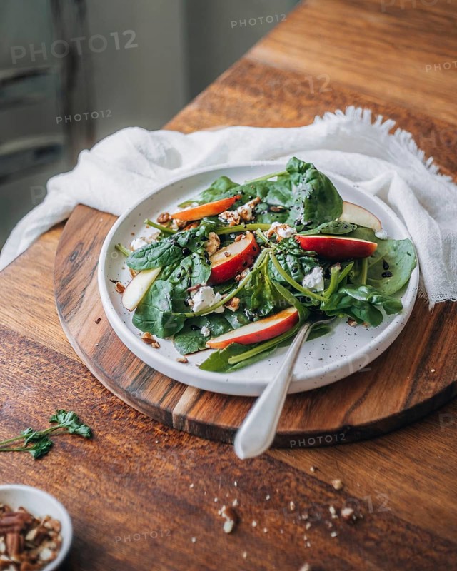 A vibrant and nutritious spinach salad topped with crisp apple slices, scattered pecans, and crumbled cheese, served on a rustic wooden board