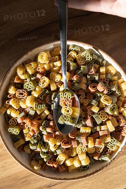 Top view of a bowl filled with multicolored, number shaped pasta being served with a spoon. The number 2025 prominently displayed on the pasta signifies the new year