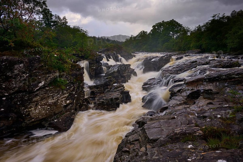 A torrential river in a rocky environment, nestled in nature and covered by a dark sky, River Orchy, Eas Urchaidh, Bridge of Orchy, Scotland, United Kingdom, Great Britain