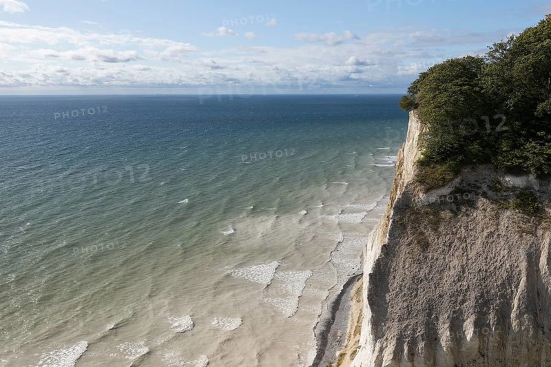 White chalk cliffs at Hundevængsfald with a view of the Baltic Sea towards Møn Lighthouse under a clear blue sky. Møns Klint, Region Sjælland, Denmark