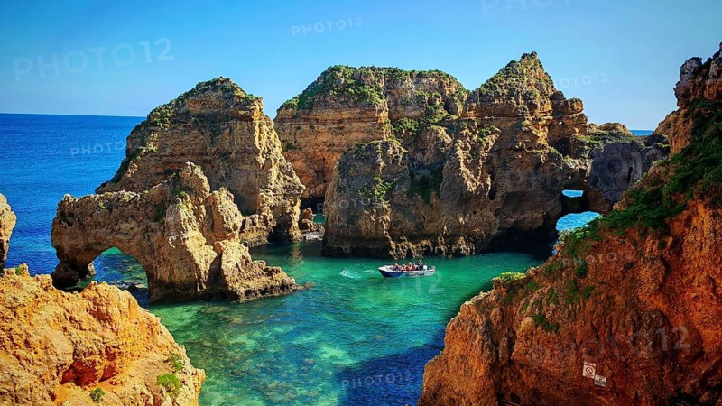 Natural wonder with rock arches and clear turquoise water, in which a boat with tourists, Ponta da Piedade, Lagos, Algarve, Portugal