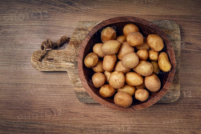 A rustic wooden bowl filled with freshly harvested small potatoes sits on a wooden cutting board, showcasing natural textures and earthy colors