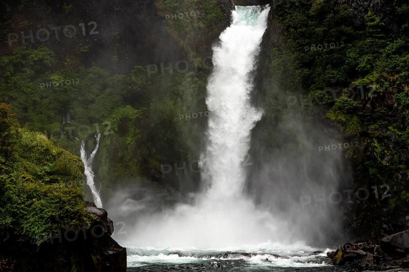 Waterfall falls over dark rock face in Gumpe, surrounded by thick rainforest with clouds of fog, Huilo Huilo Biological Reserve, de los Ríos Region, Chile