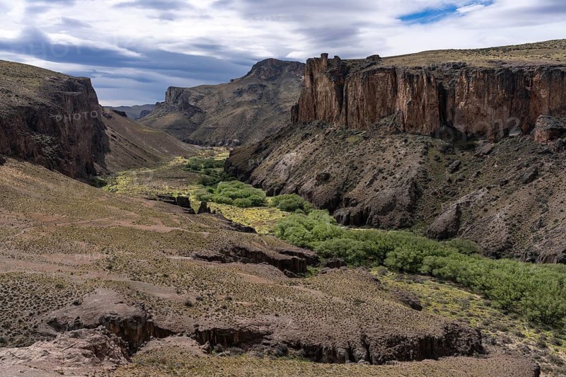 Río Pinturas canyon with steep rock walls and green valley floor, cloudy sky, Cueva de las Manos, Santa Cruz Province, Argentina
