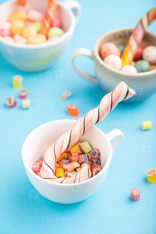 Heap of multicolored caramel candies in cups on blue pastel background. close up, side view, selective focus