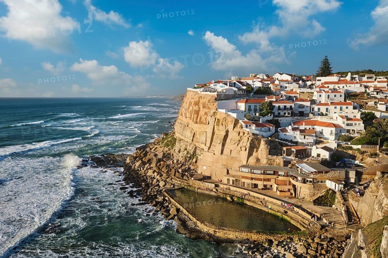 Azenhas do Mar is a picturesque fishing village perched on a cliff by the Atlantic Ocean. Colorful houses overlook the sea, creating a beautiful view under a bright blue sky