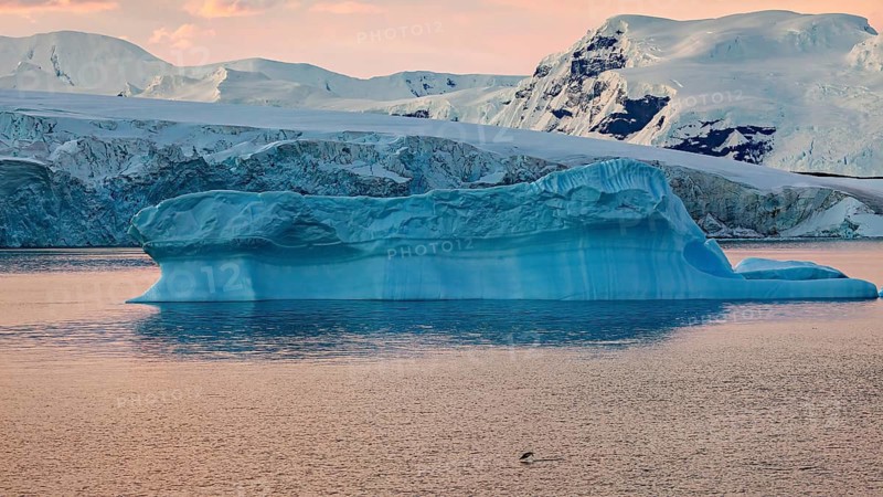 Large blue iceberg drifting in calm sea water at sunset, icebergs in the Southern Ocean in Antarctica