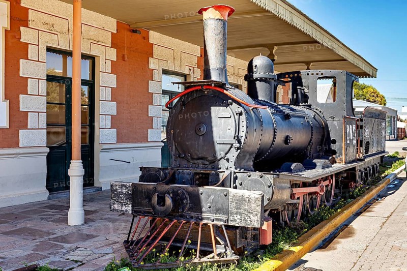 Old steam locomotive stands on tracks next to a historic railway station with brick architecture, old steam locomotive at Puerto Madryn railway station in Argentina