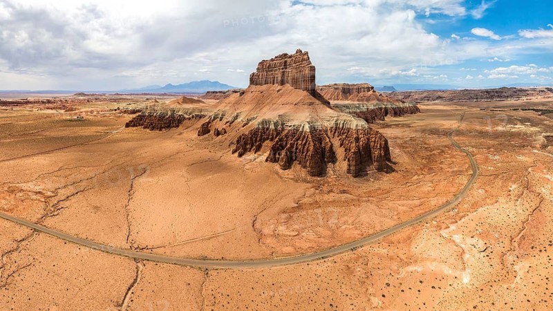 A panoramic aerial shot of Goblin Valley State Park, showcasing the unique sandstone formations and arid landscape under a cloudy sky, with a winding road cutting through the desert