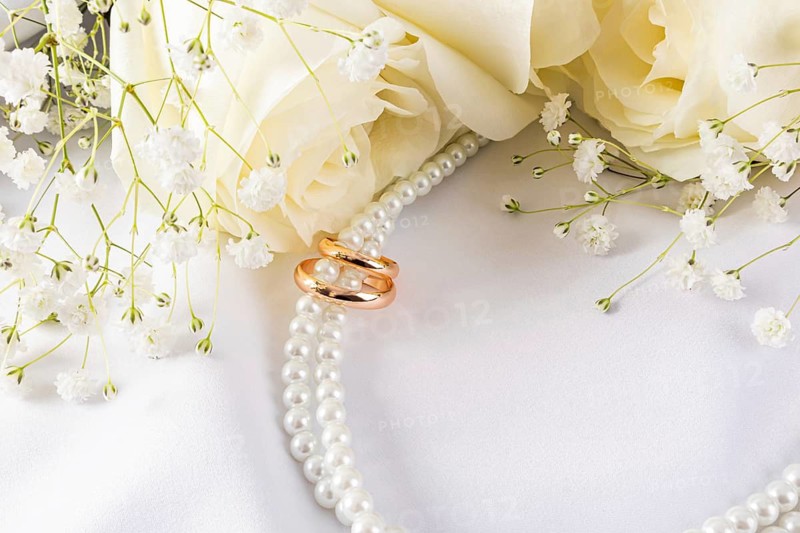 Elegant wedding rings are showcased with delicate white flowers and pearls against a soft white fabric backdrop, creating a sophisticated and romantic atmosphere