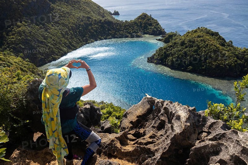 An ecotourist admires the breathtaking view of crystal-clear blue waters and lush green islands in the Raja Ampat Archipelago, West Papua, Indonesia