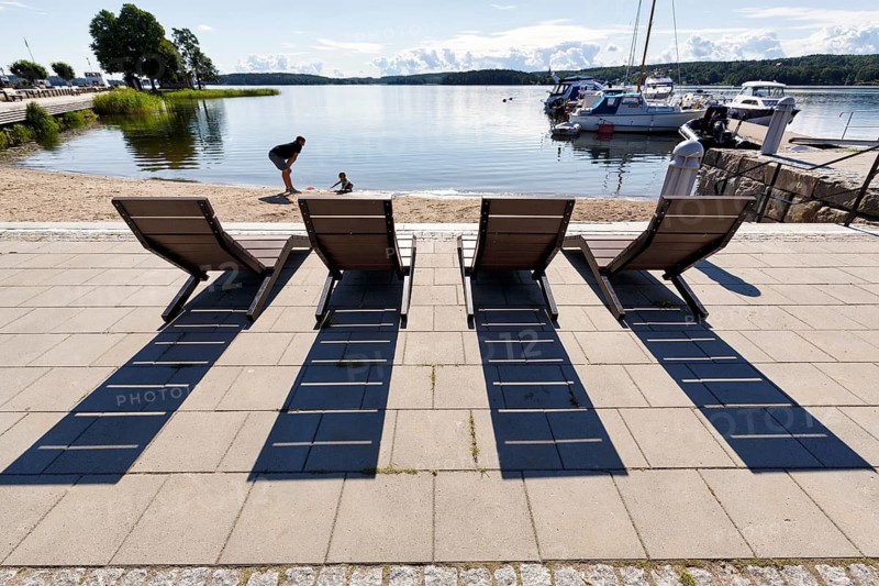 Four wooden deckchairs with views of Lake Mälaren, long shades of sunshine, Mariefred marina in summer, Lake Mälaren, Strängnäs, Södermanland County, Sweden