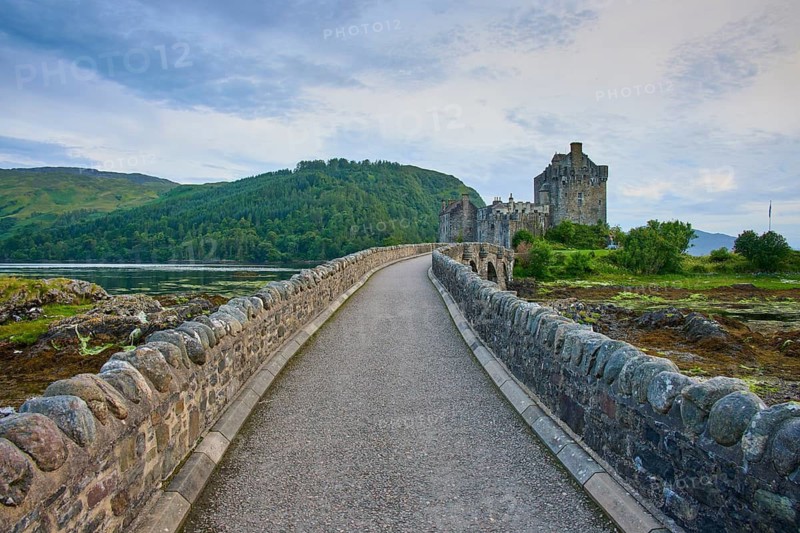 A rocky path leads to a historic castle surrounded by lush nature and rolling countryside, Eilean Donan Castle, Dornie, Kyle of Lochalsh, Scotland, United Kingdom, Great Britain
