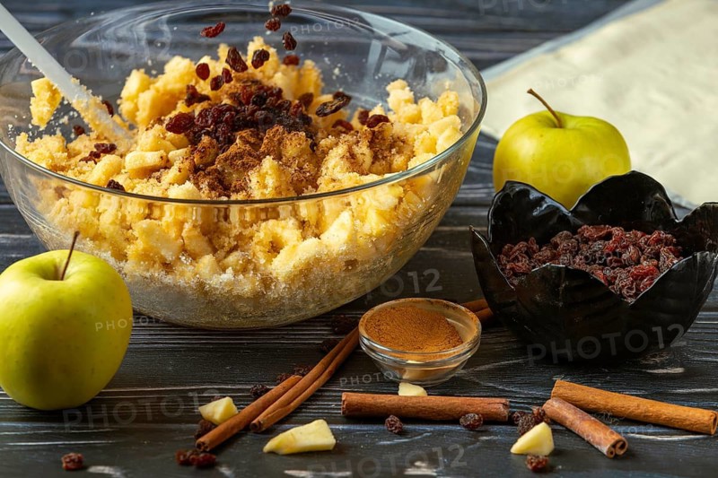 Raisins fall into a bowl with apple pieces, cinnamon and other ingredients for apple strudel