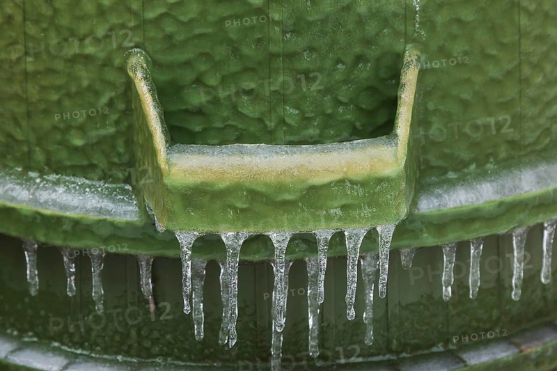 Handle on upside down green PVC and rubber thrash can covered with thick sheet of ice and hanging icicles after freezing rain in late winter, Quebec, Canada