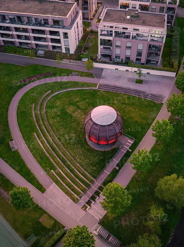 Aerial view of a modern wooden sphere on a green area, surrounded by buildings and symmetrical paths, Forstkugel, Nagold Black Forest, Germany