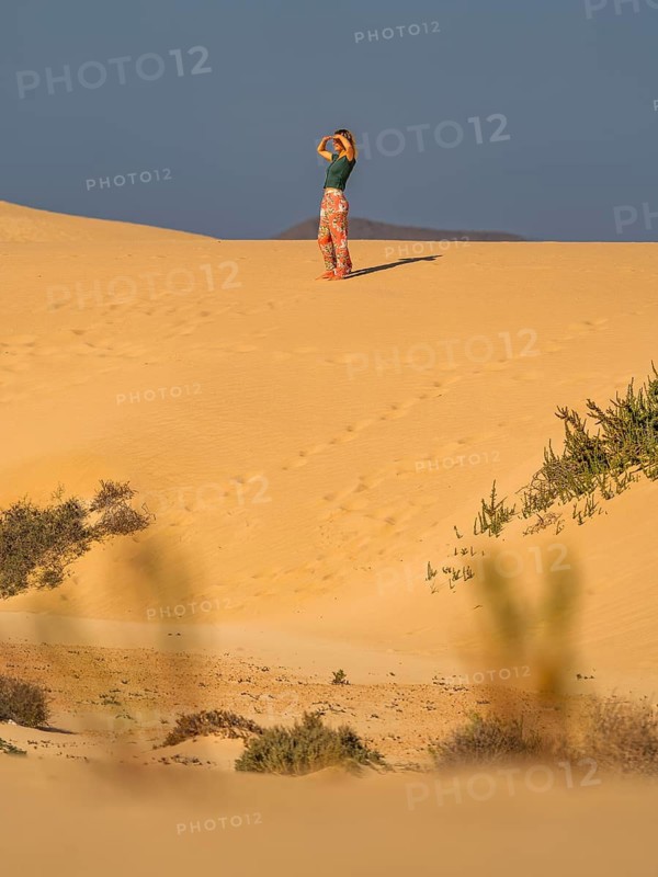 A lone woman stands on the dunes of Fuerteventura, Canary Islands, Spain. Surrounded by vast sandy landscapes and clear skies, capturing the essence of adventure and solitude