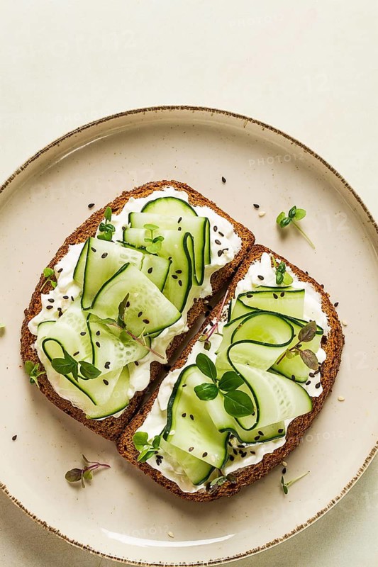 Breakfast, cereal bread sandwiches, cream cheese, sliced cucumber, with micro greenery on a light table, close-up, top view, selective focus, no people