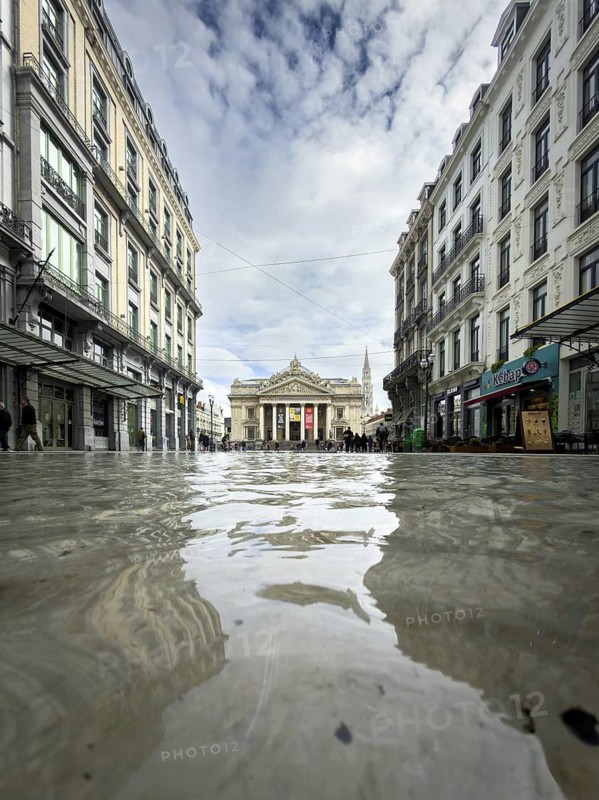 Neoclassical building of the former Brussels Stock Exchange (La Bourse) at the end of a street canyon with reflection in a fountain, Brussels, Belgium