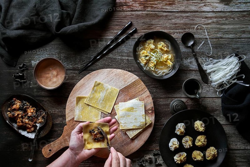 Top view of anonymous woman preparing wonton soup on a wooden table